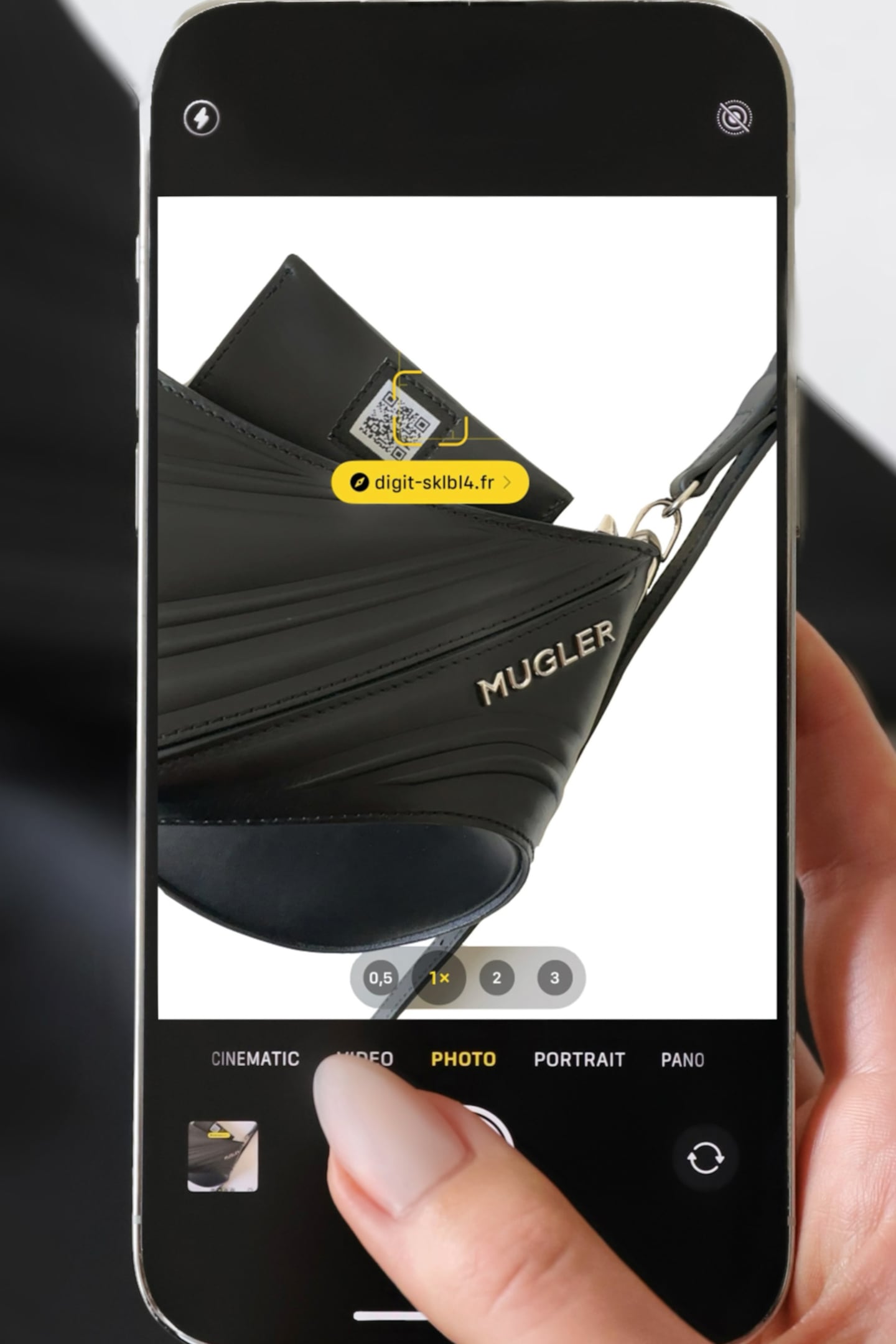 A hand holds a phone over a QR code attached to a leather card peeking out of a Mugler handbag.